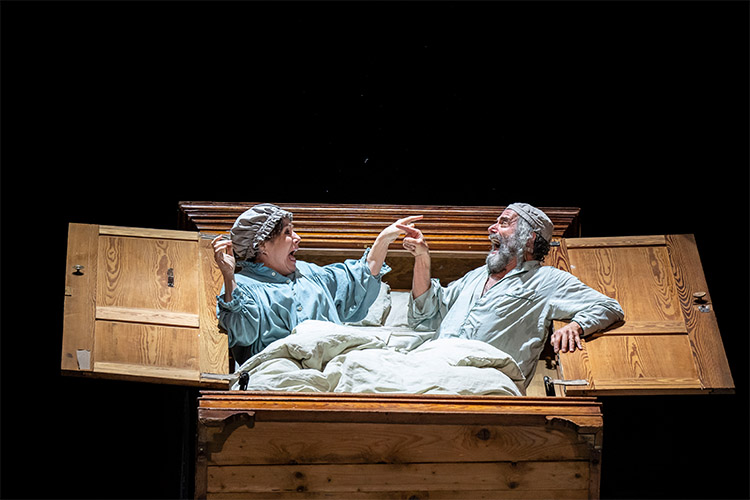 Golde and Tevye are in their pajamas enthusiastically singing and pointing to one another.